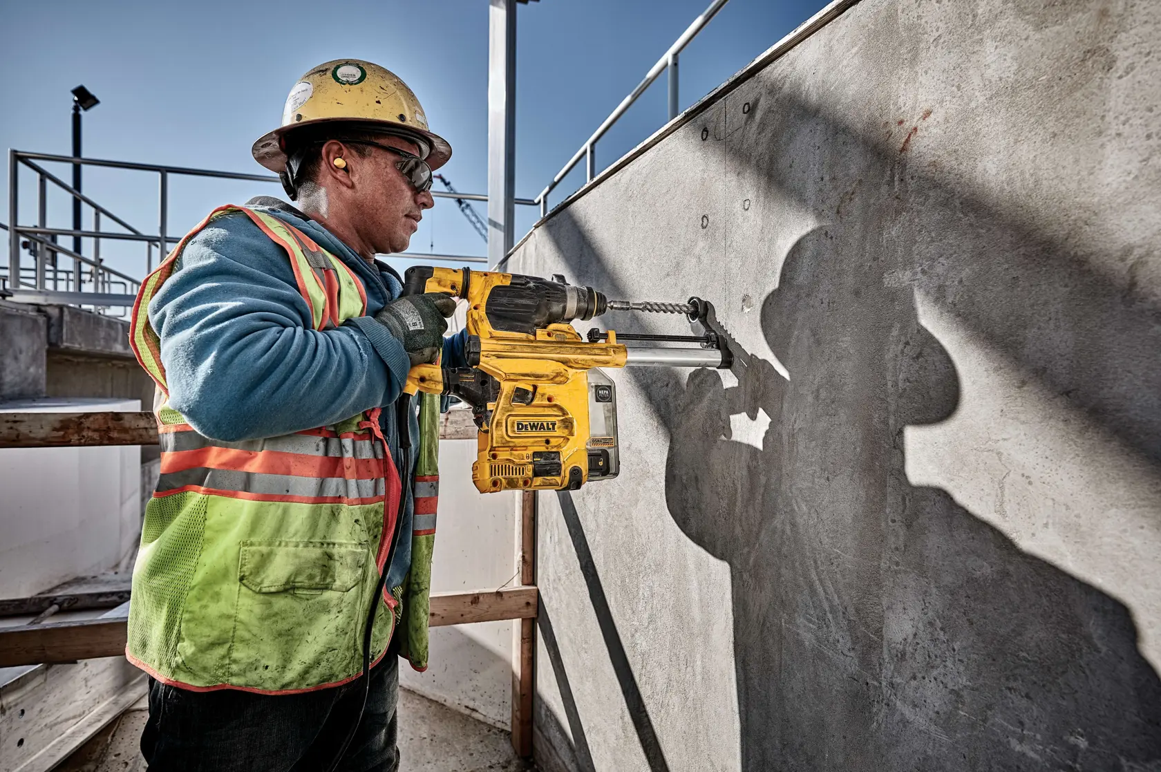 Ein Bauarbeiter mit Helm und Sicherheitsweste verwendet einen DEWALT D25333K Schlagbohrhammer, um eine Betonwand auf einer Baustelle im Freien zu bohren.
