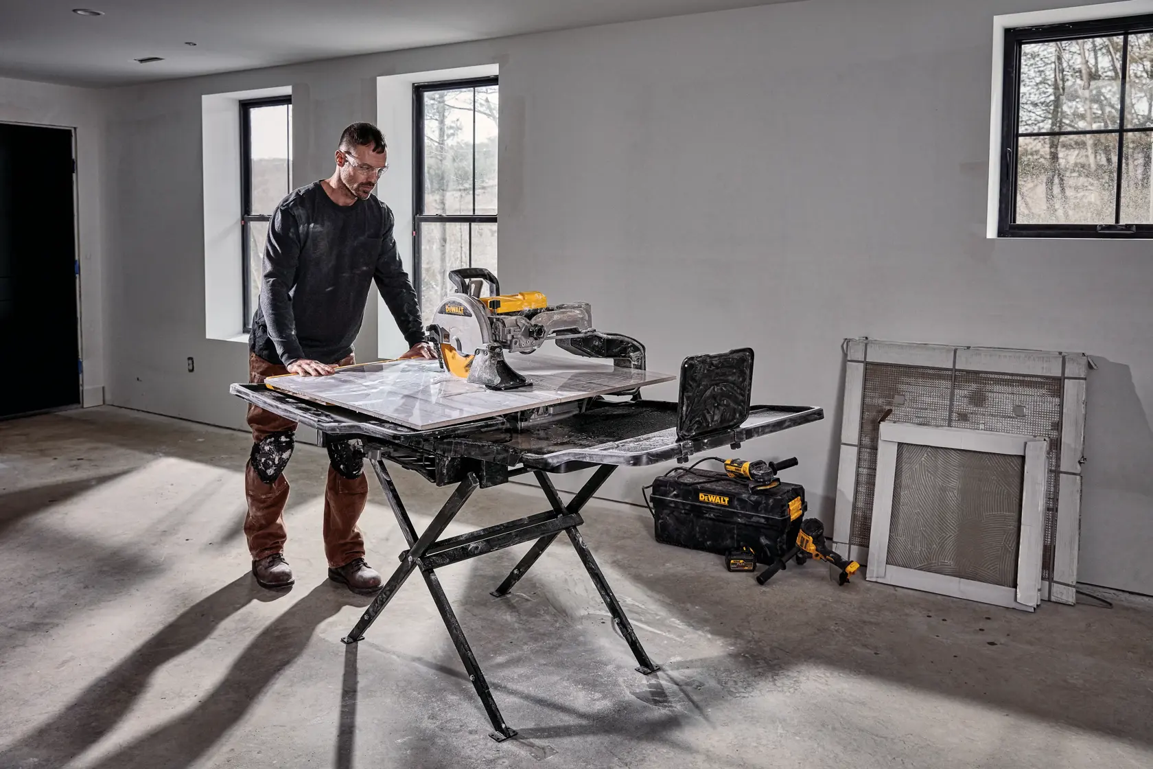 A person is cutting a large tile with a DEWALT tile saw. The saw blade is spinning and the person is guiding the tile carefully with their hand.
