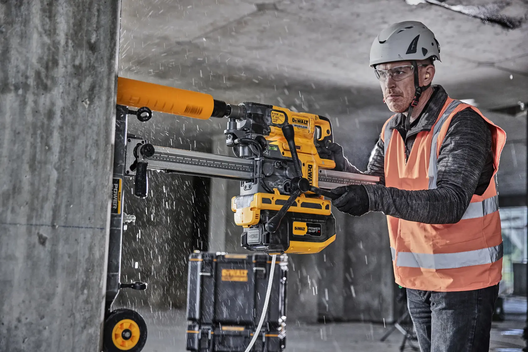 Worker uses a DEWALT drilling tool on a concrete wall; wearing safety gear and an orange vest.