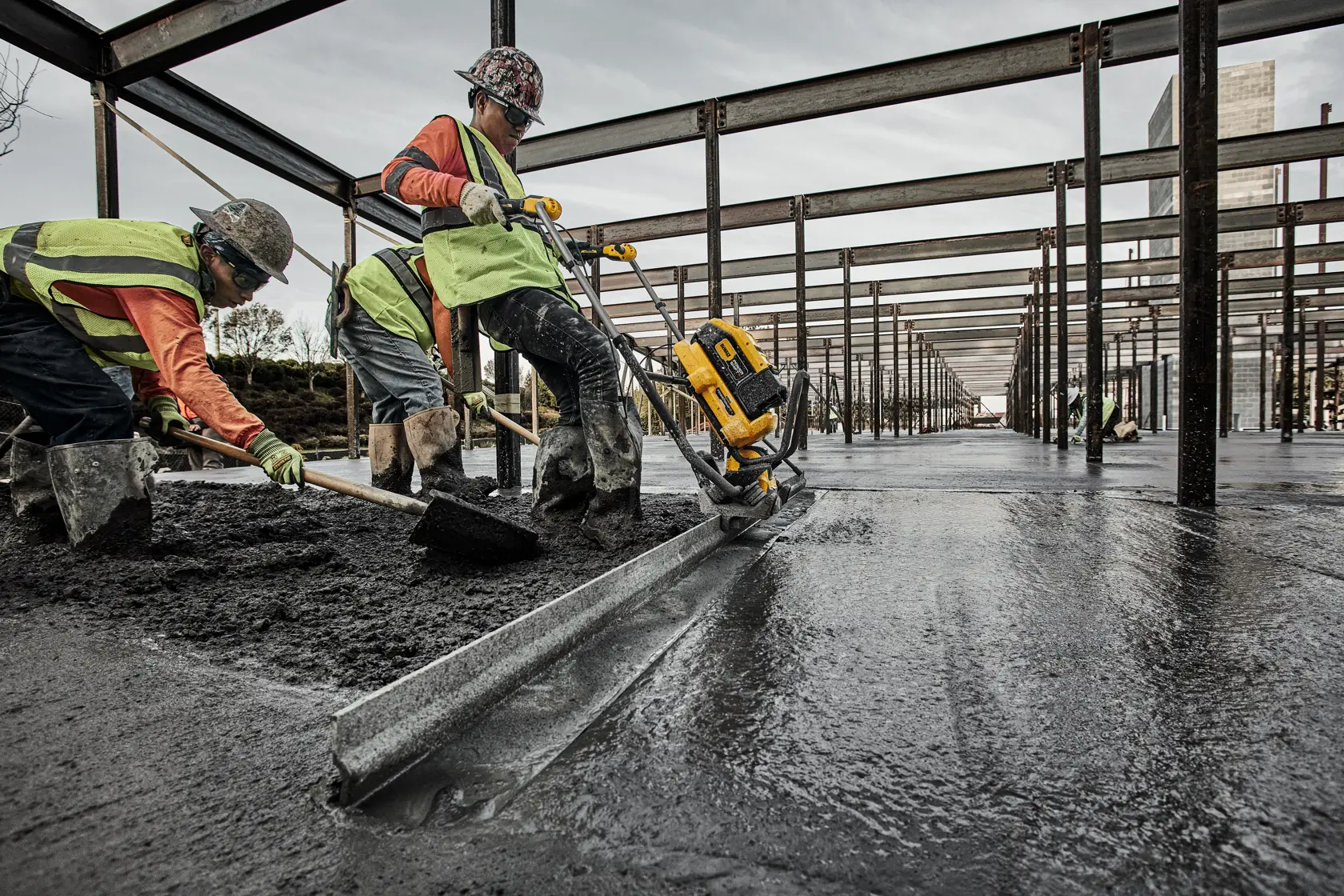 Workers use a DEWALT power tool to smooth wet concrete in a large building construction site.