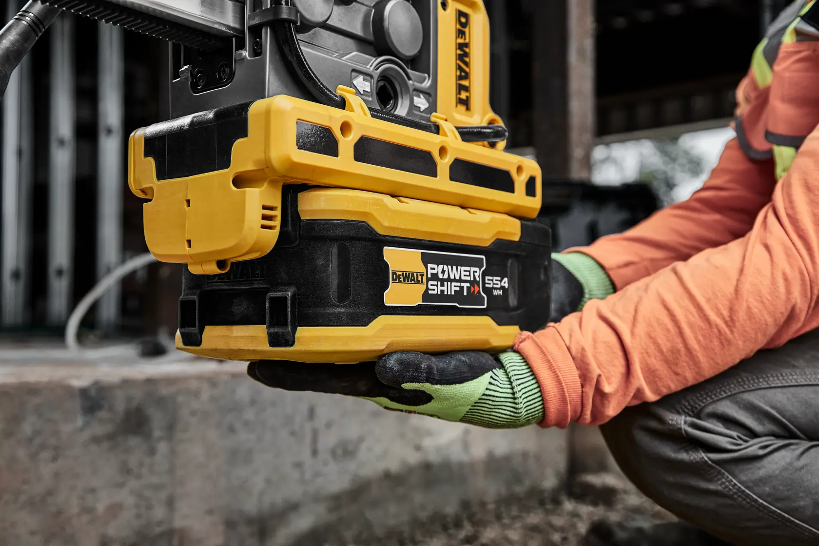 Persona lleva herramienta DEWALT amarilla en obra con refuerzo de acero y estructuras sin terminar.
