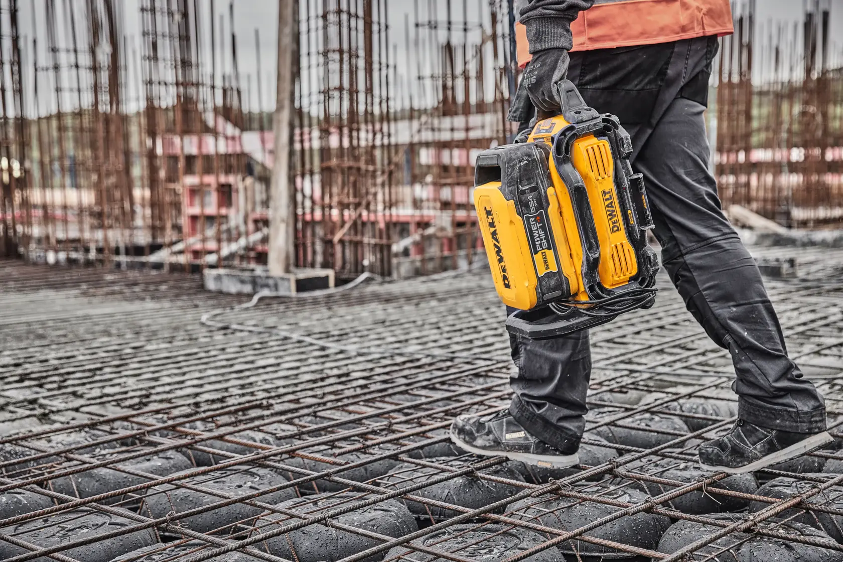 Persona camina en obra llevando un maletín de herramientas DEWALT.