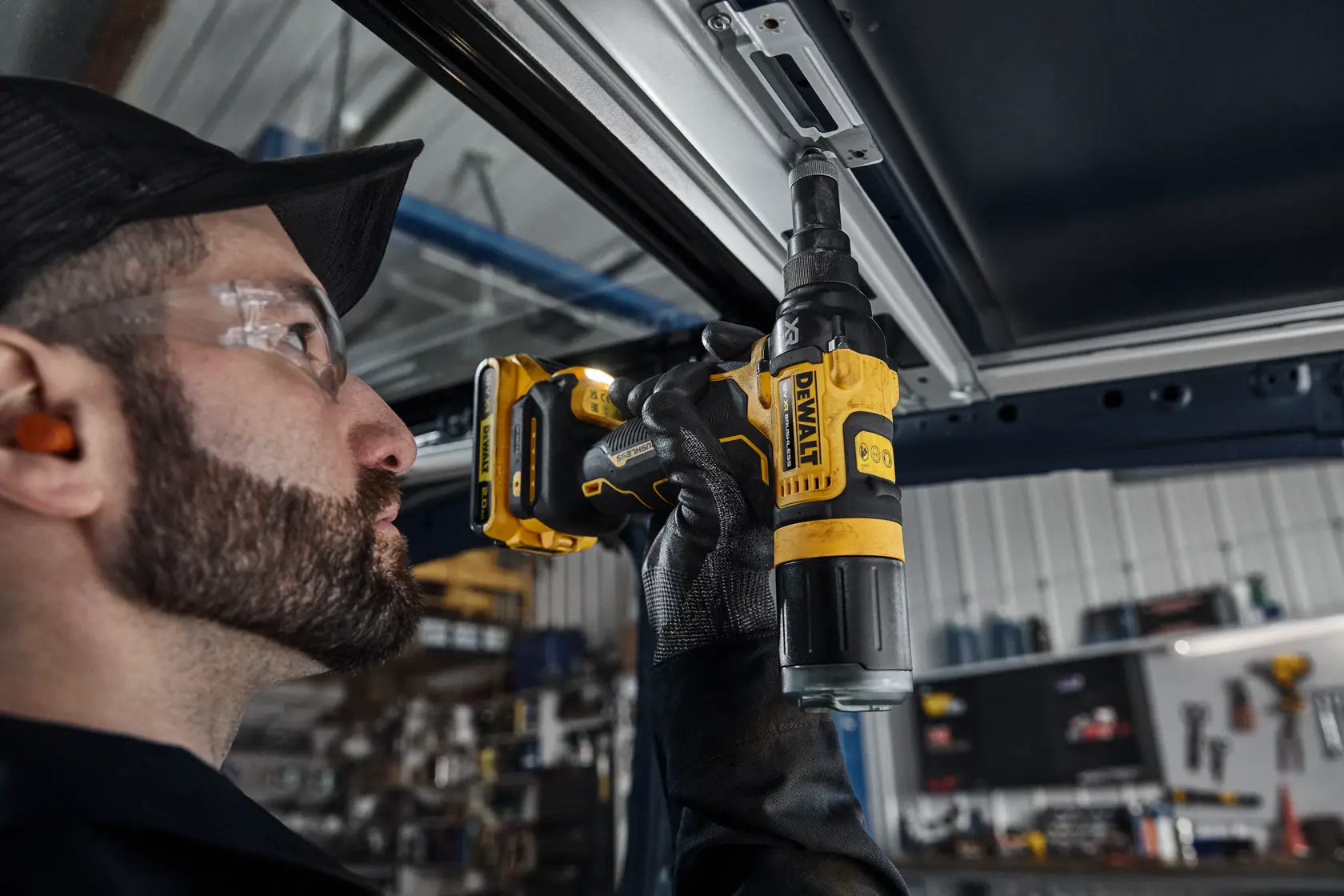 A person using a DEWALT DCF403NT cordless screwdriver to fasten a screw into a metal frame in a workshop setting. The focus is on the tool and the user’s gloved hand.