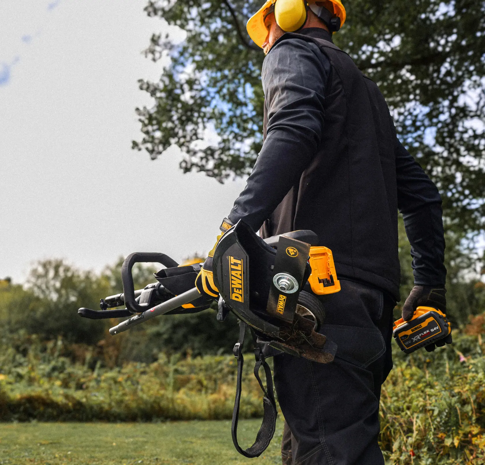 DEWALT DCMASED57X1, DCMASED9N Freischneider, draußen gehalten von Person mit Schutzausrüstung, Fotografie.