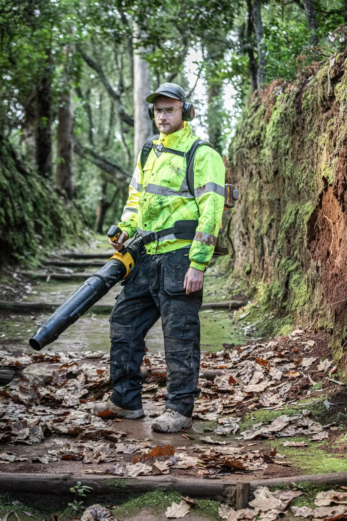Trabajador usa soplador DEWALT DCMBBL800N-XJ, DCMBBL800N afuera. Fotografía. Lleva equipo de seguridad.