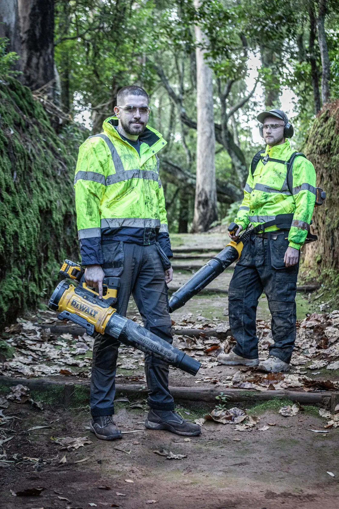 Dos personas con sopladores DEWALT, DCMBBL800N-XJ, DCMBBL800N, chaquetas reflectantes, al aire libre.