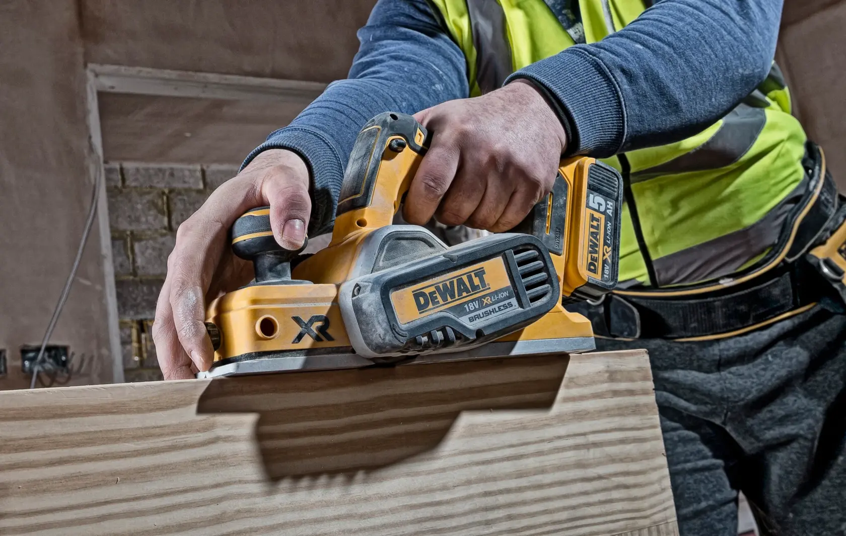 Photo of DEWALT DCP580N cordless planer in use on wood, close-up view of tool and user's hands.