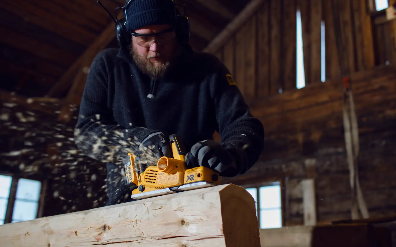 Photo of DEWALT DCP580P2 cordless planer used on timber, wood shavings flying in workshop.