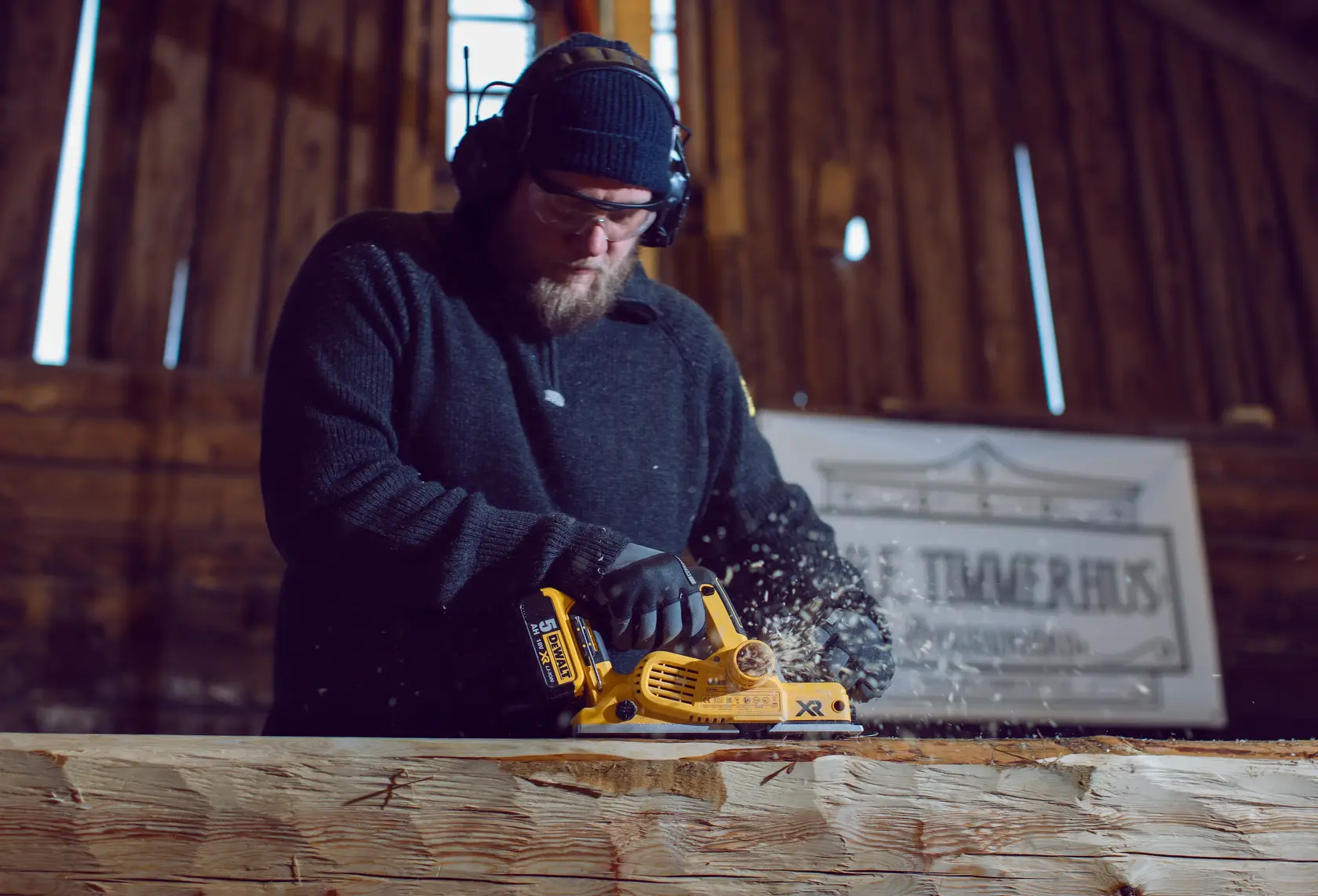 Photo of worker using DEWALT planer DCP580P2 to smooth a wooden beam indoors, wood chips flying.