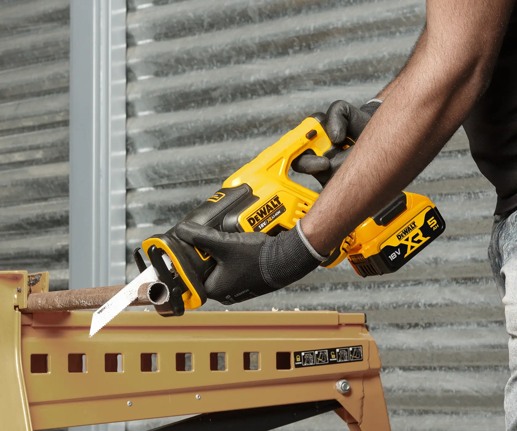 Photo of DEWALT DCS367P2 reciprocating saw cutting a metal pipe, yellow and black, with gloved hands.