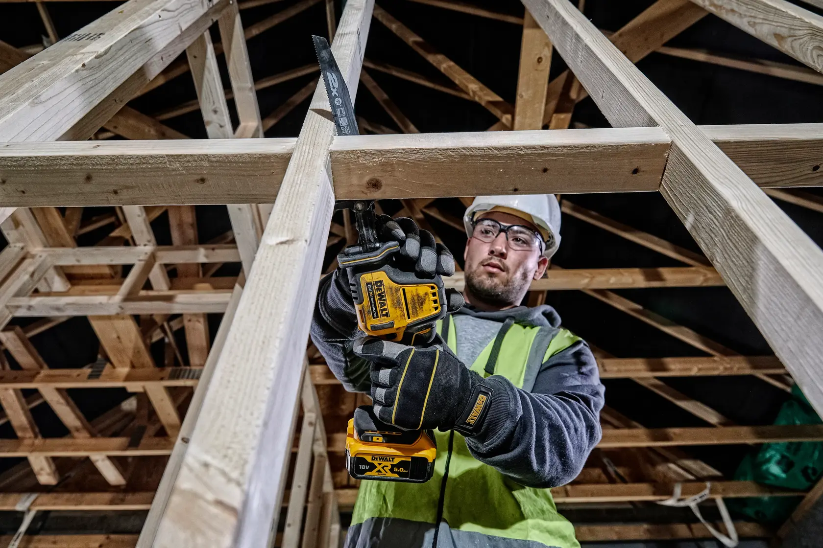 Photo of worker using DEWALT DCS369NT cordless saw to cut wood frame at construction site.