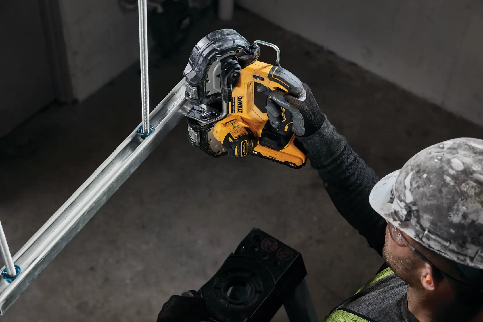 Photo of DEWALT DCS377NT cordless band saw cutting metal pipe, worker in gloves and helmet operating tool.