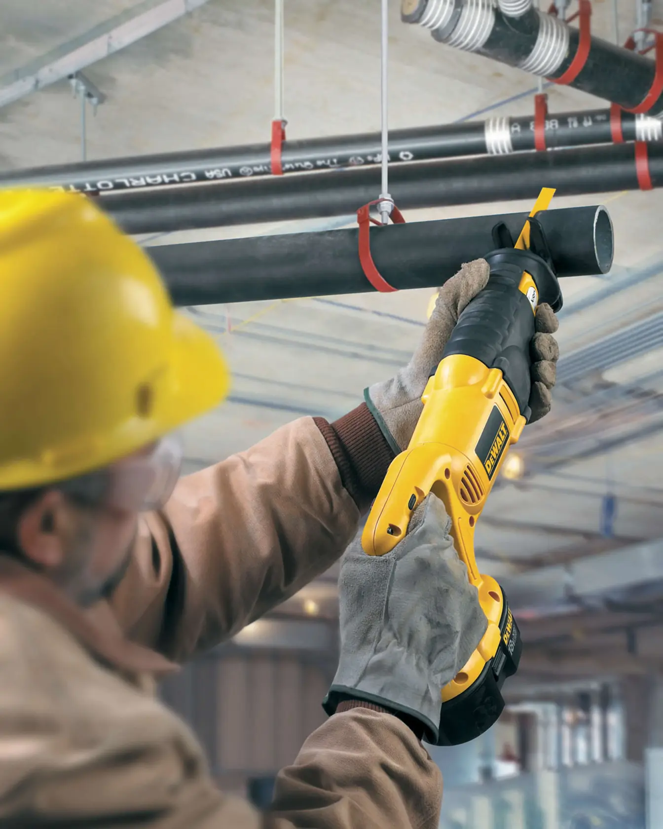 Trabajador corta un tubo negro suspendido con una sierra DEWALT en un entorno industrial.
