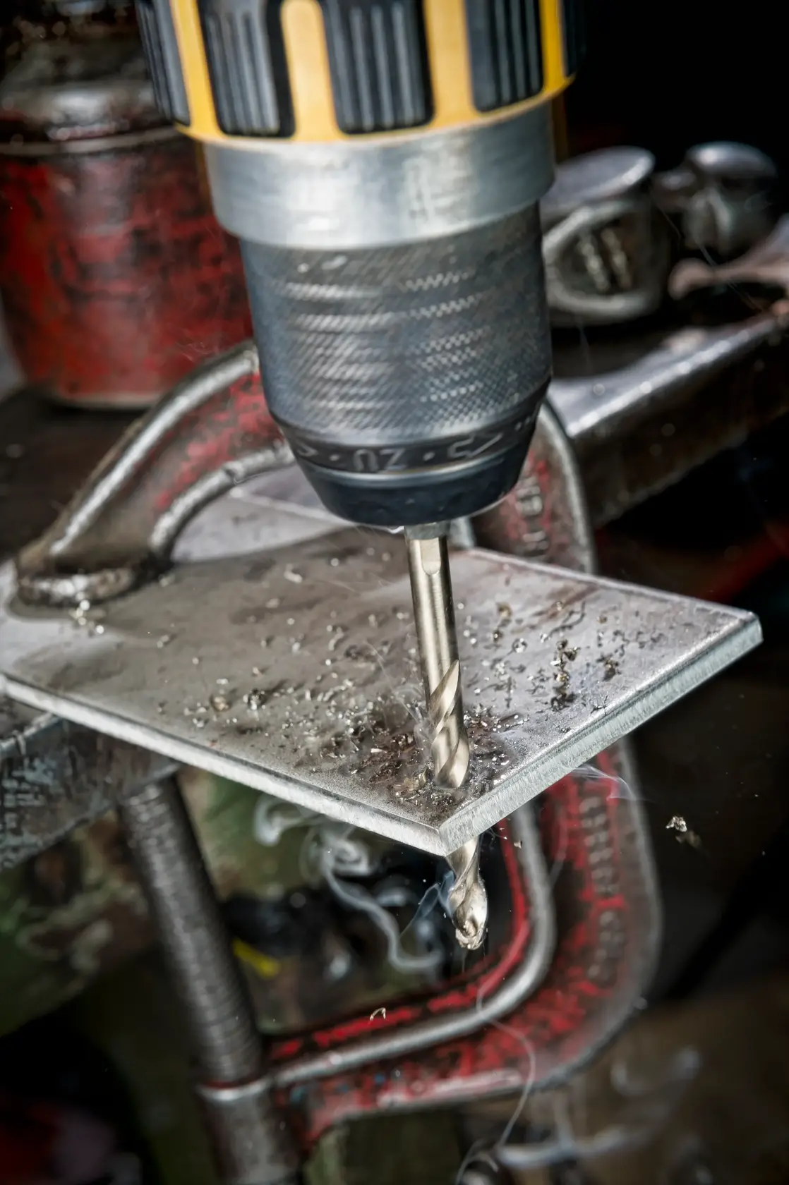 DEWALT drill with metal drill bit making a hole in a metal sheet held by a clamp, metal shavings visible.