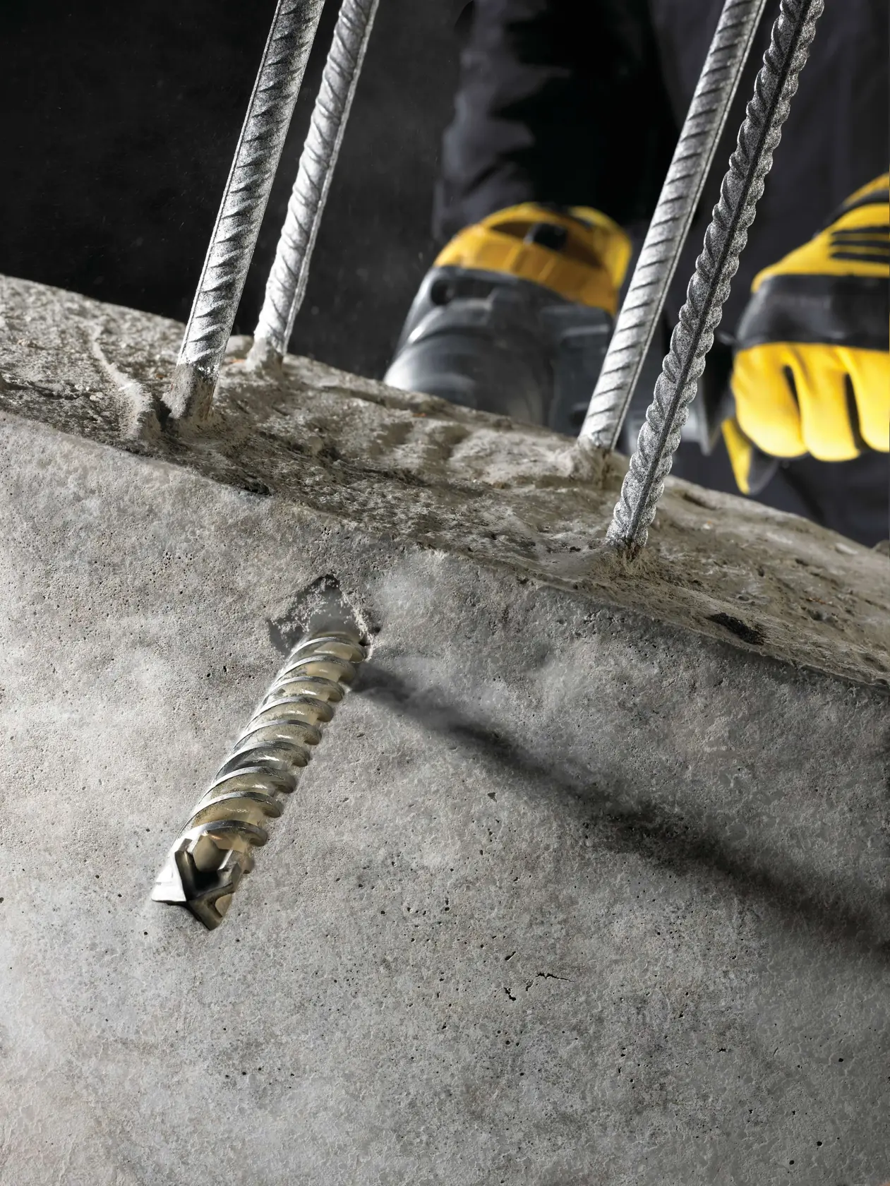 Trabajador usa taladro DEWALT en obra con estructura de acero y equipos bajo cielo azul.