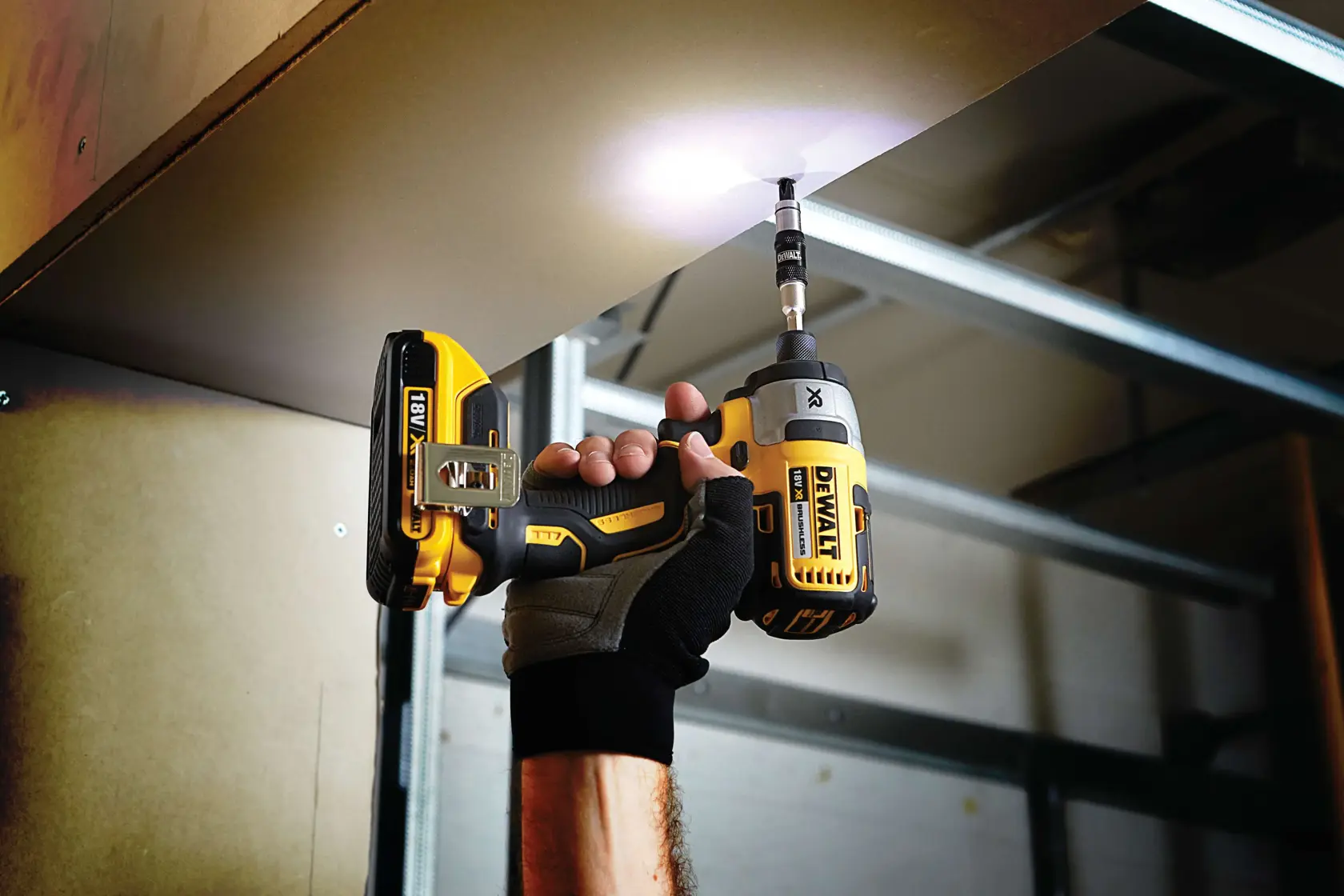 Person using a DEWALT cordless drill to drive a screw into a ceiling panel in an indoor construction setting.