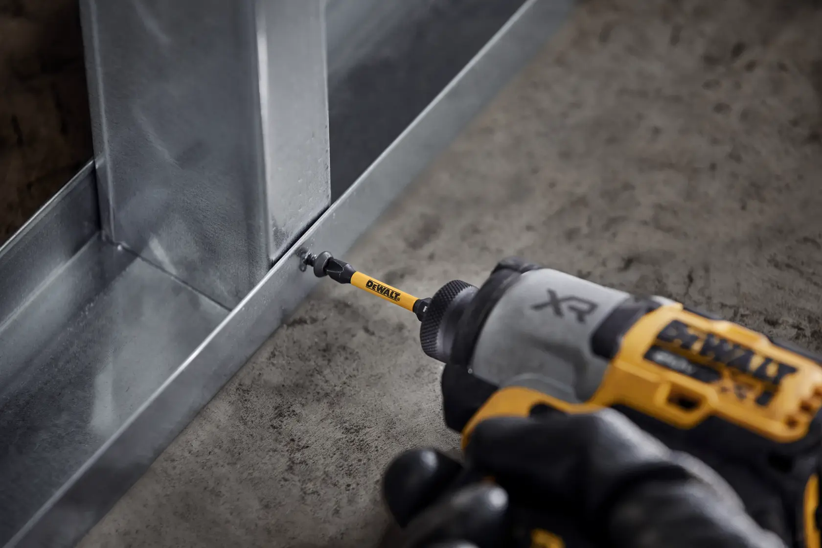 DEWALT drill driving a screw into a metal frame, close-up view of the tool and construction surface.