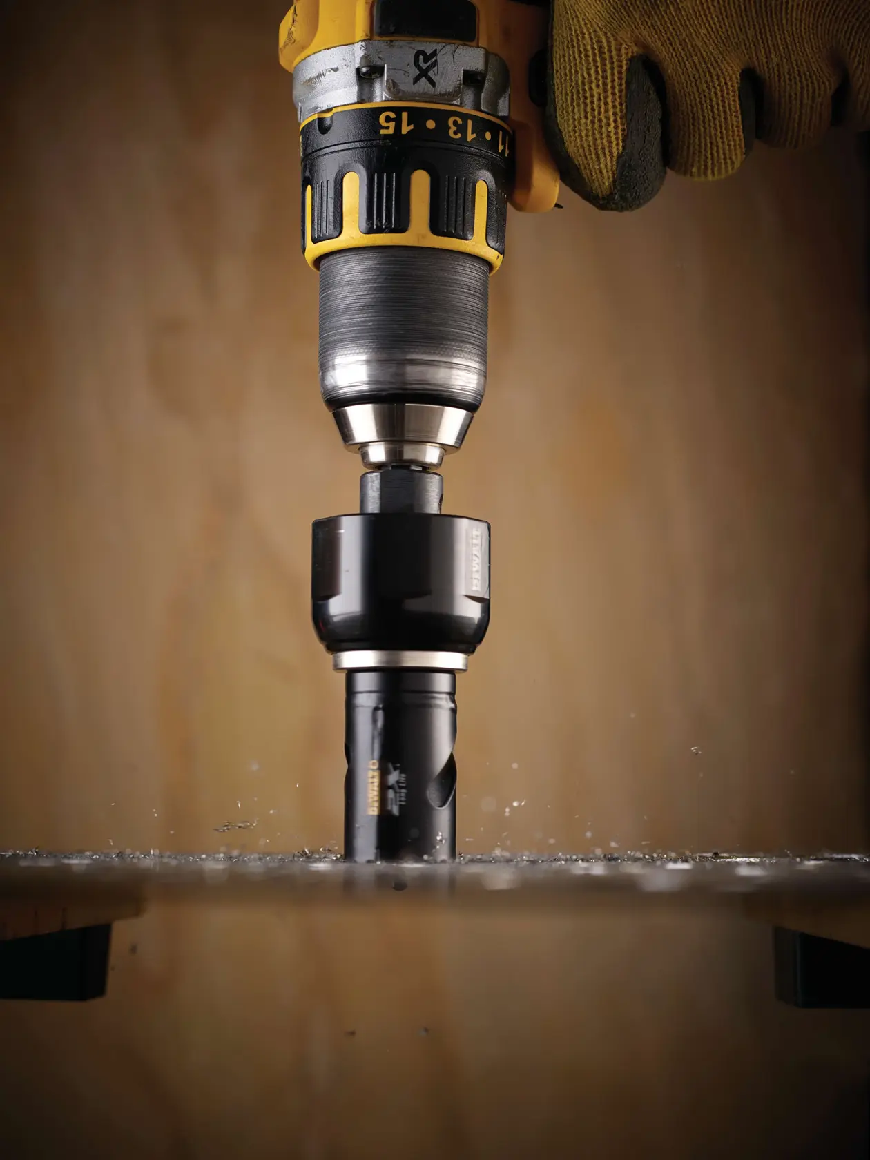 DEWALT drill with a hole saw cutting through a surface, held by a gloved hand, with metal shavings visible.