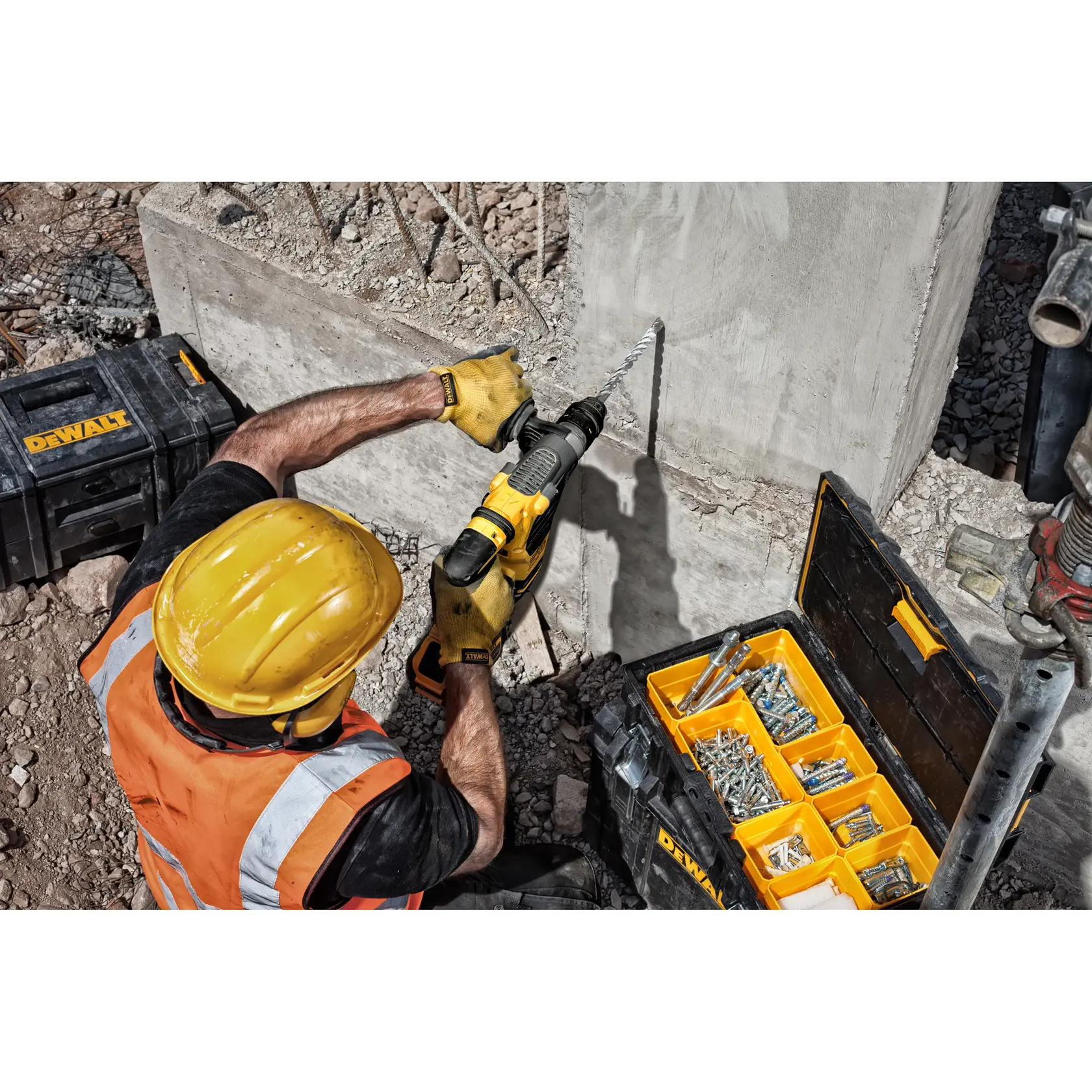 Trabajador perfora concreto con taladro DEWALT, cajas de herramientas y fijaciones visibles.