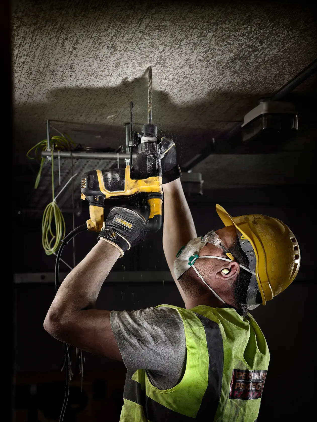 Trabajador usa taladro DEWALT en el techo, con equipo de seguridad y chaleco reflectante.