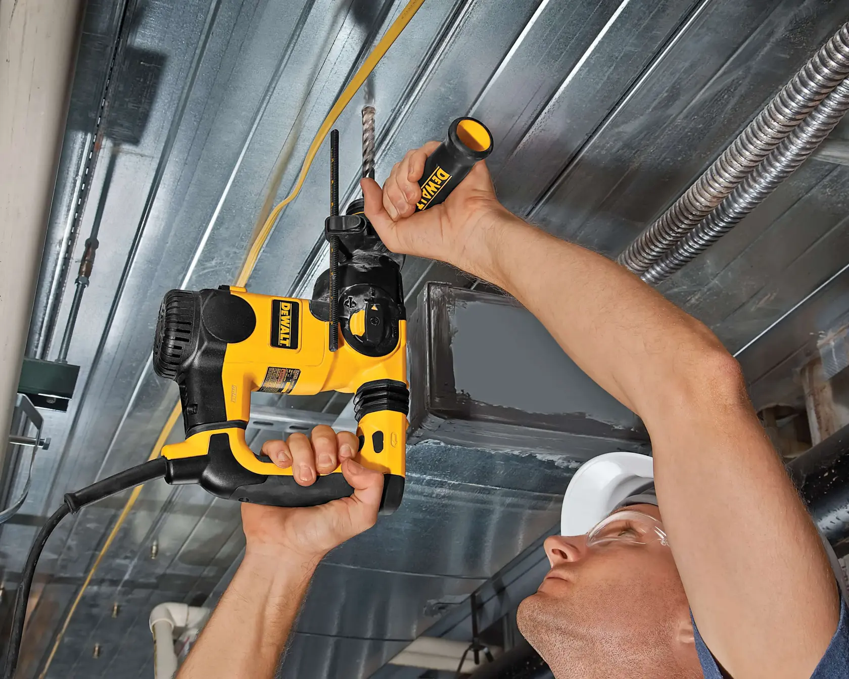 Persona usa taladro percutor DEWALT para perforar techo metálico, sujetando la herramienta con ambas manos.