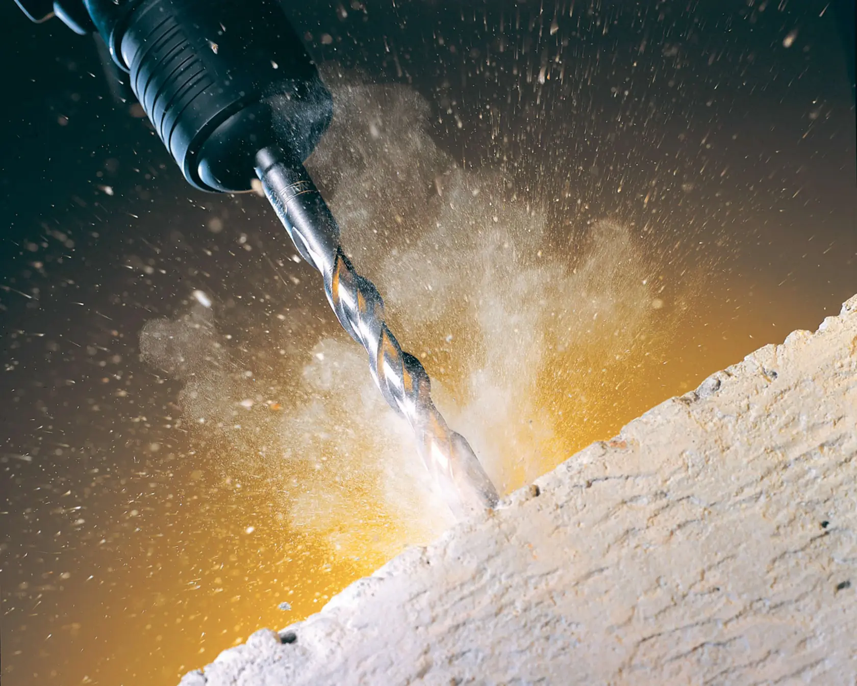 Primer plano de una broca DEWALT perforando concreto, con polvo y escombros dispersos.