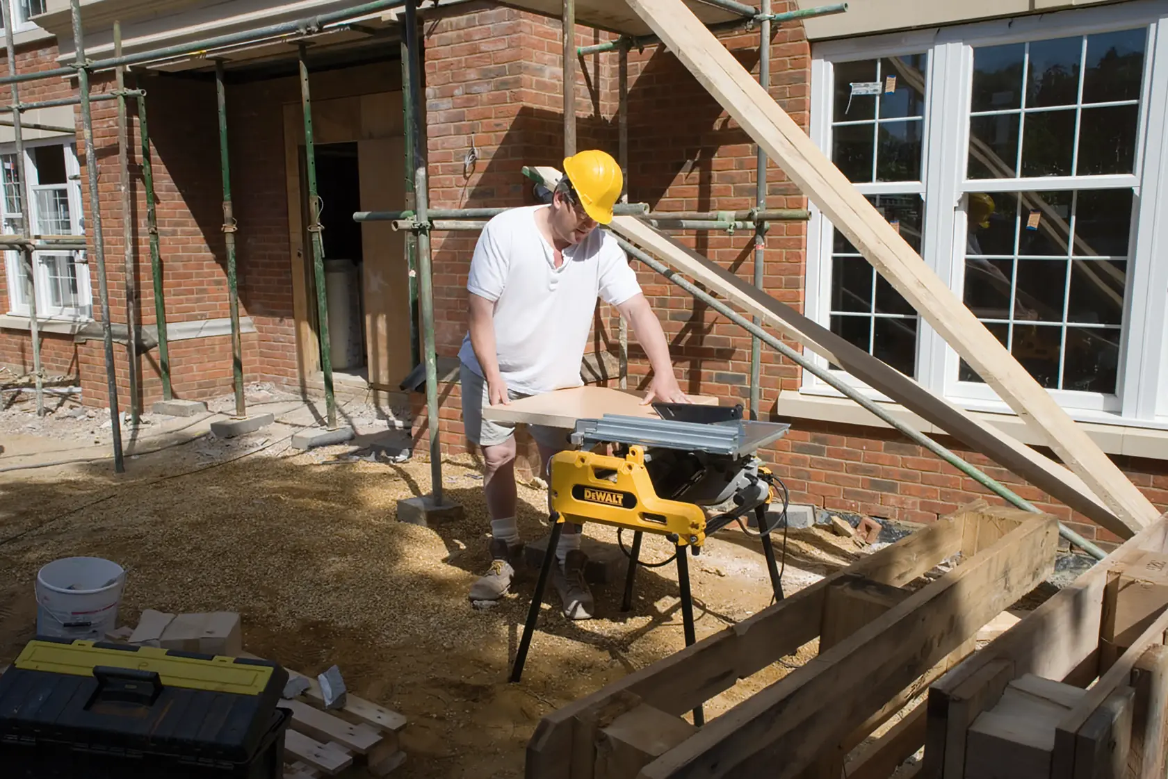 Worker using a DEWALT DW743N saw outdoors at a construction site with wooden planks and scaffolding nearby.
