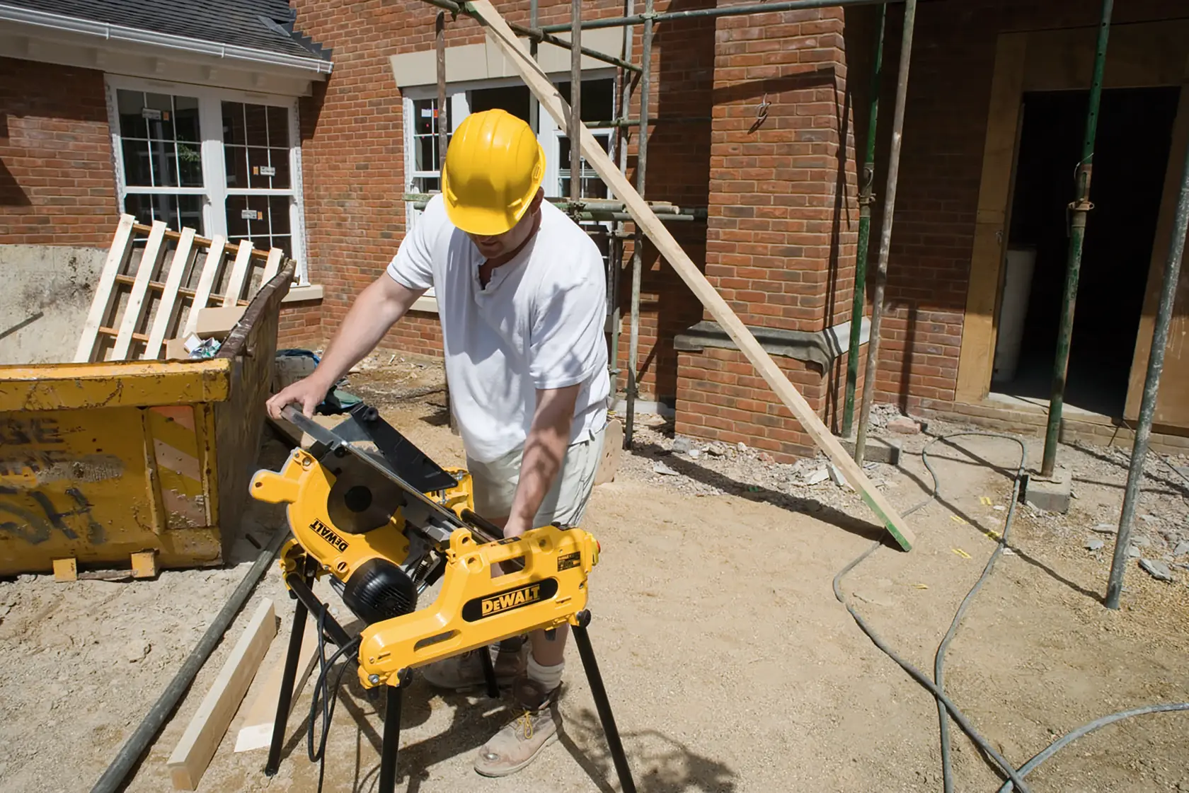 Person uses DEWALT DW743N saw on construction site outdoors near brick building.