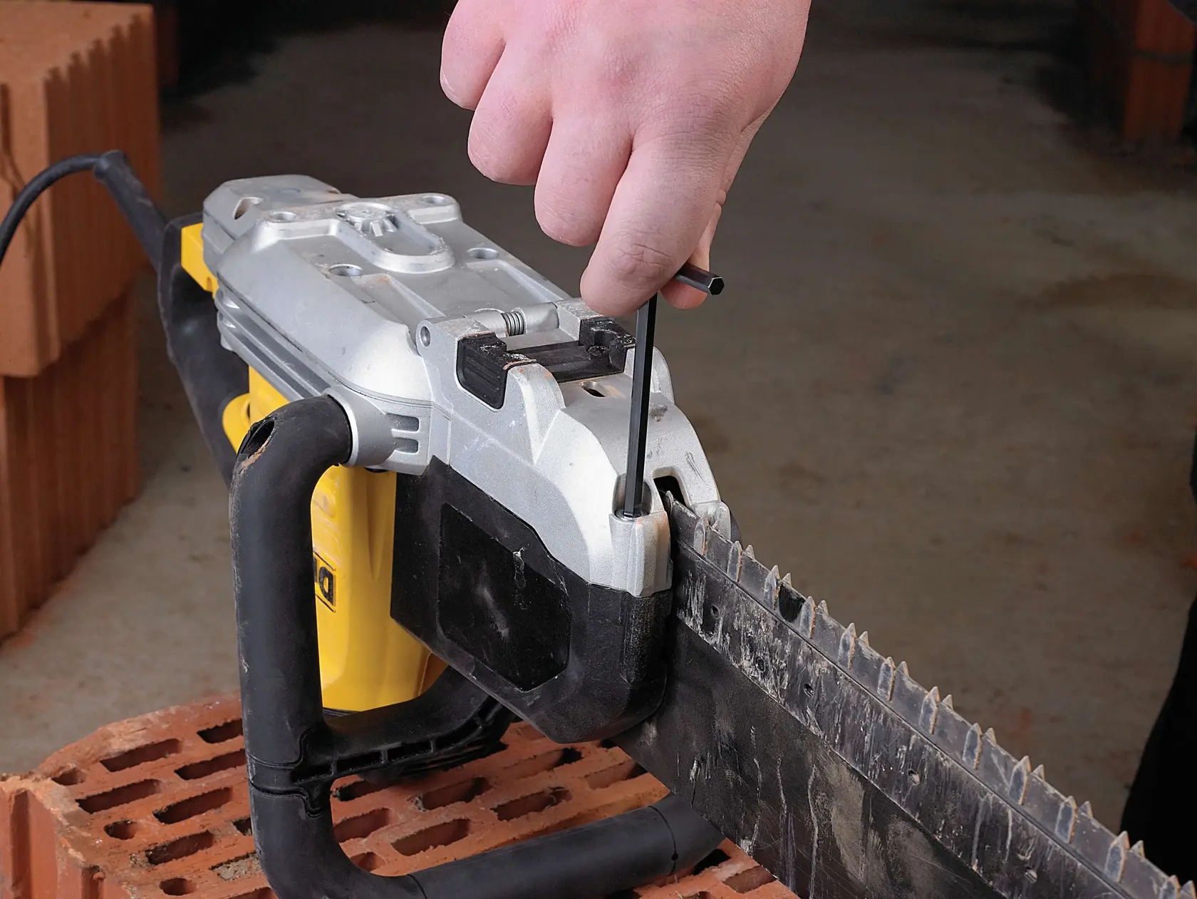 Hand uses tool to adjust blade on a DEWALT power saw placed on a brick.