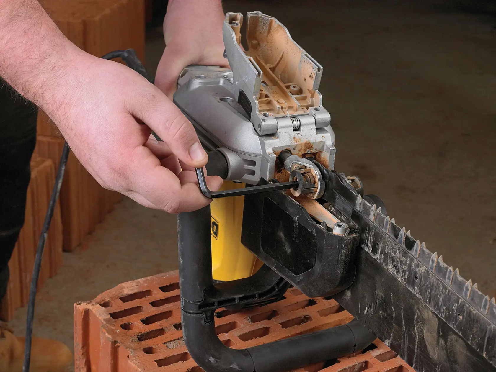 Person uses a hex key to adjust a DEWALT electric masonry saw placed on a brick.