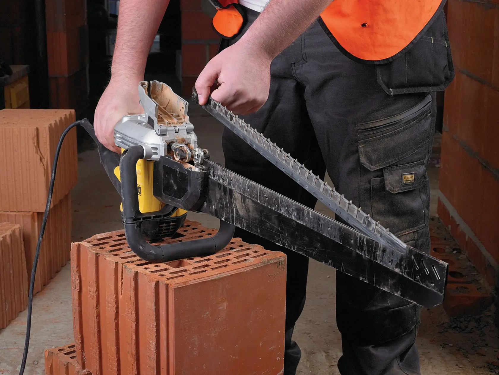 Person uses a DEWALT electric masonry saw to cut a large clay brick on a construction site.