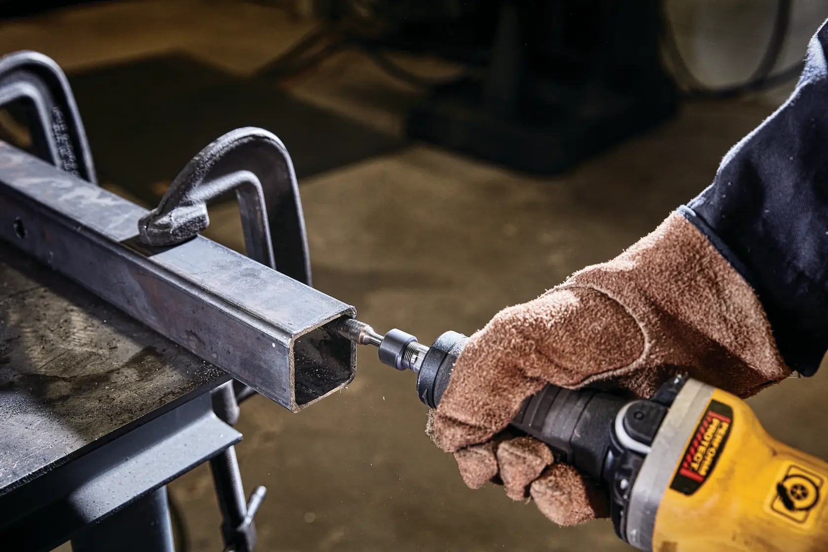 Photo of DEWALT DWE4997 angle grinder used on metal pipe, worker with gloves holding tool close-up.