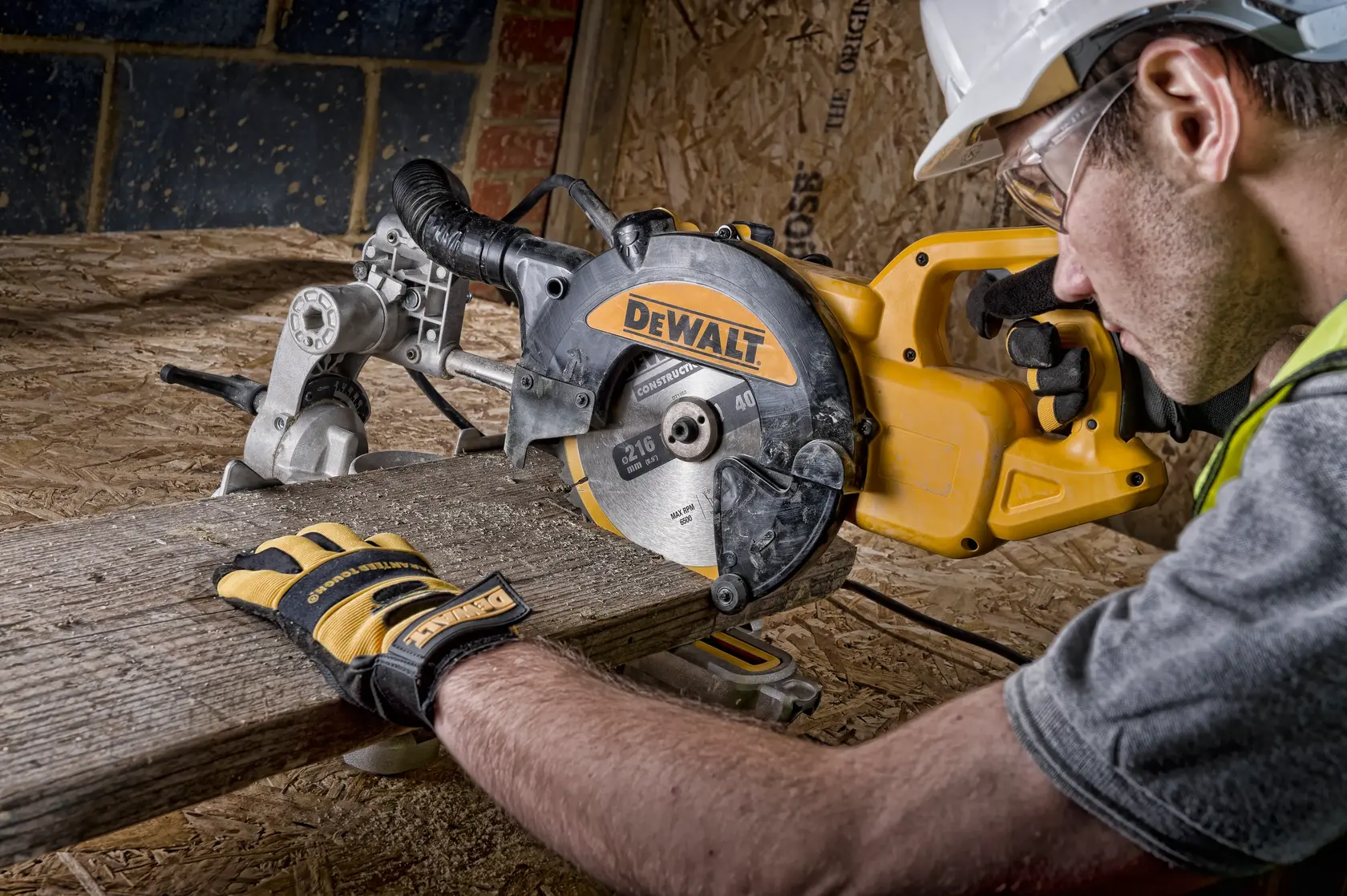 A DEWALT DWS773 saw is used to cut wood. Person wearing gloves and safety gear operates on a construction site.