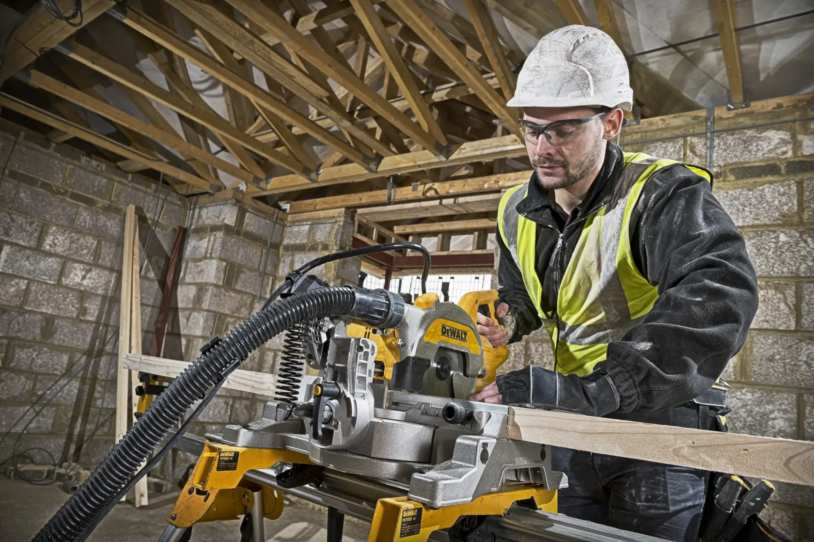 Worker using DEWALT DWS777 saw to cut wood at construction site. Safety gear and hi-vis vest worn.