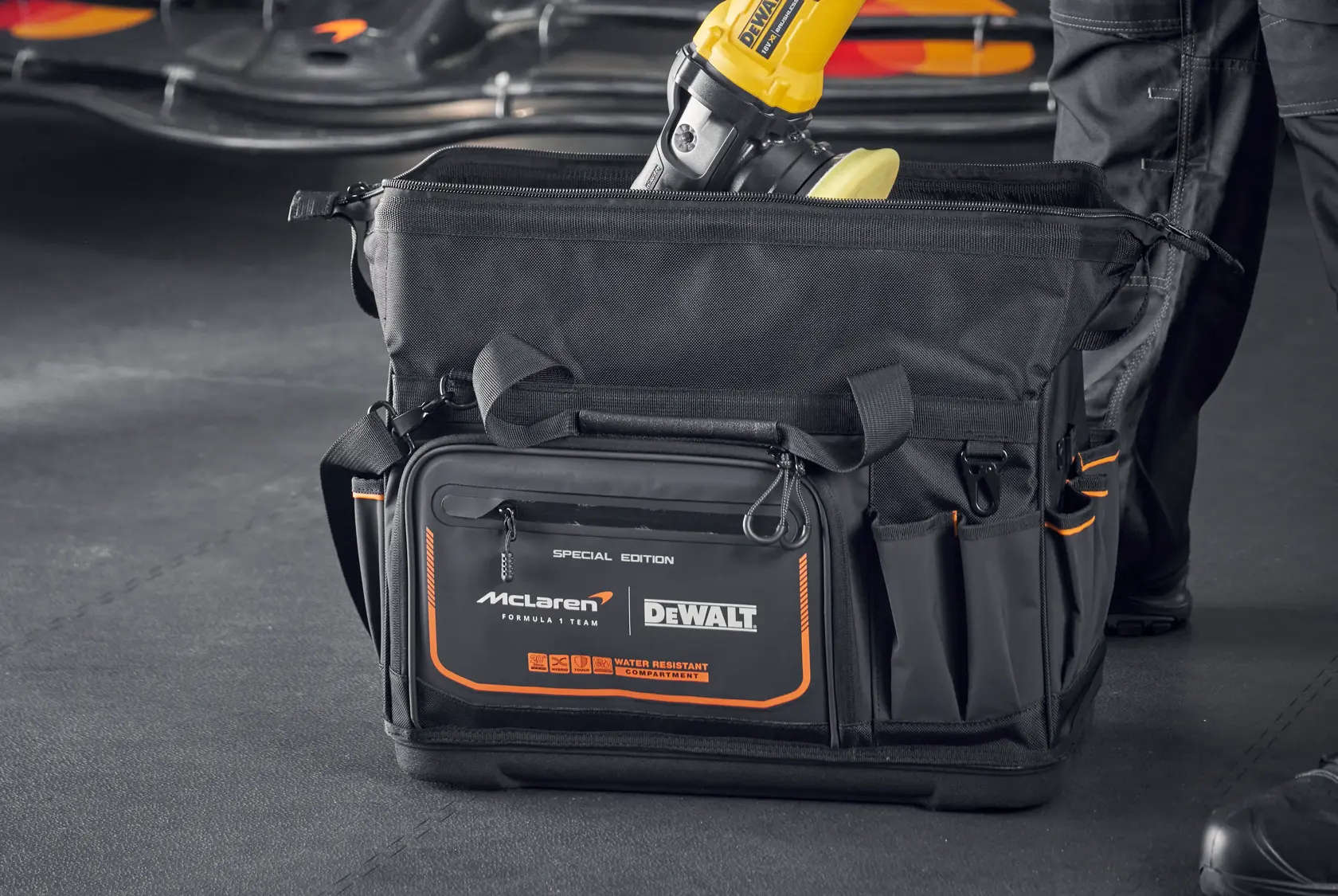 Bolsa de herramientas DEWALT McLaren negra con detalles naranjas y compartimentos, mostrada en taller.